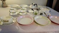 Full lot view on table showing all pieces including plates, cups, teapot, pie plates, and casseroles