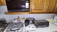Countertop view showing multiple small kitchen appliances including a bread maker, a slow cooker, a toaster oven, and a white hand mixer with cord.