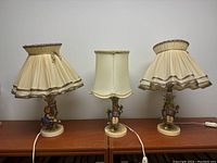 Full frontal view of the three Hummel lamps showing the figurines on the bases and fabric lampshades.