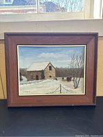 Framed oil painting showing winter farm scene including a stone farmhouse, horses, and trees under a blue sky.