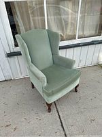 Front and side angle of vintage green wingback armchair showing general shape, seat cushion, and armrests.