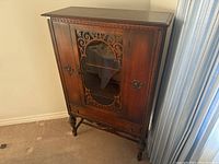 Full frontal photo of walnut china cabinet showing the carved wooden door with glass and turned legs.