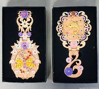 Two boxed ornate metal jointed mirrors with colorful enamel and rhinestone floral and animal motifs on metal frames.