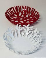 Two geometric modern style fruit bowls, one white enamel Alessi and one red plastic Mueller, seen from angled front view