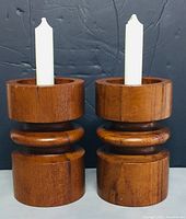 Front view of both teak candle holders each holding a white candle showing wood finish and proportions.