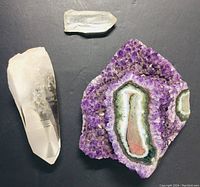 Photo showing three natural crystals on a black background: a large clear quartz point, a smaller clear quartz point, and a flat amethyst cluster with a colorful geode center.