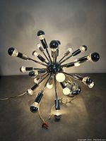 Spherical Sputnik-style chrome chandelier with various lit bulbs on pendant fixtures shown against plain background.