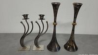 Four metal candlestick holders in total, two with curved double arms on square bases (Dansk) and two tall trumpet-shaped holders with gold-tone rings (Karshi).