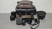 Overall lot: bag with padded interior, flash unit, power adapter, round lens cases and accessory case displayed on table