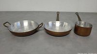 Photo showing full set of three mini copper cookware pieces: a small saucepan with long handle, a frying pan with long handle, and a sauté pan with two side handles.