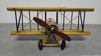 Front view of vintage yellow biplane toy airplane with wooden propeller and wheels.