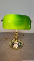 Front view of vintage bankers desk lamp with green glass shade and brass base, showing color and height.