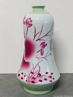 Front view of the porcelain vase showing pink floral and lotus designs with green base and neck.