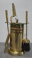 Front angle of vintage brass fireplace tool set showing brush, shovel, poker, tongs, and holder.