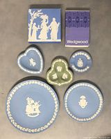 Five Wedgwood Jasperware dishes arranged with two assortments of packaging boxes, showing a mix of blue and green jasperware with classical white relief decoration