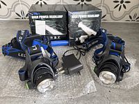 Two high power LED headlamps, one charger, one blue rechargeable battery, and packaging boxes shown on bubble wrap.