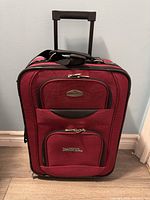 Front view of red Cambridge suitcase with two zippered pockets and handle on top.