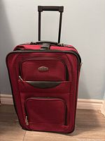 Front view of red Cambridge suitcase with two zippered front pockets and extended telescoping handle