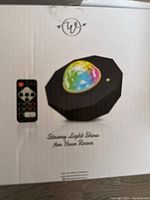 Photo of the boxed projector showing the product and remote control image with text 'Stream Light Show for Your Room'