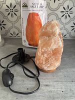 Salt lamp with power cord, showing natural pinkish salt rock texture and packaging in background