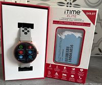 Open box showing the iTime Elite Fitness Smart Watch in rose gold with gray adjustable strap, displayed with screen icons visible, alongside the packaging noting $49.97 price and compatibility with iOS/Android.