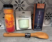 Photo showing all four items: Camelbak water bottle, Owala bottle boot, Foodville milk frother in box, and Good Grips wooden spoon.