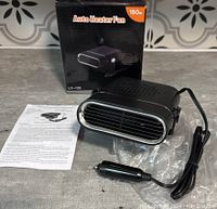 Auto heater fan front view with cigarette lighter plug visible on table surface. Instruction sheet and packaging box are included in background.