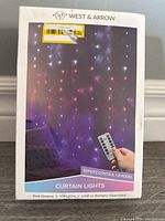 Front image of the West & Arrow LED curtain lights box showing the product name, lighting effects, and remote control.