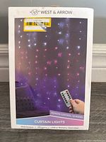 Box front showing the West & Arrow branding, curtain lights image with remote, and main features like USB or battery operation and 8 modes.