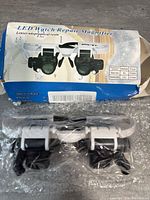 Magnifier glasses in white and black with adjustable dual lenses, shown inside original retail box with product image and details visible.