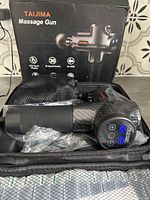 Taijima massage gun with LED touch display in carrying case and multiple massage heads in mesh pouches.