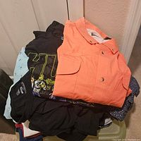 Pile of men's shirts including an orange button-up and graphic T-shirts