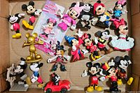 Multiple Disney figures including Mickey and Minnie Mouse in various poses and outfits arranged in a cardboard box.
