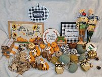 Full view of assorted fall decor items arranged on a cloth, showing scarecrows, wall hangings, pumpkins, stuffed animals, and decorative leaves.
