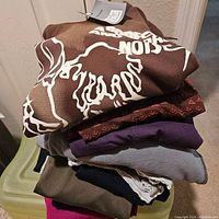 Stack of various new with tags sweaters and tops in colors brown, purple, maroon, gray, navy, and olive green.