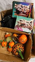 Box containing plastic pumpkins, Halloween noisemakers, and boxed Halloween figurines stacked inside a cardboard box.