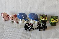 Photo of full lot showing all seven pairs of vintage salt and pepper shakers arranged in a row on a white corrugated background, including elephants, mushrooms, owls, cats, and frogs.