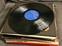Close-up of vinyl record with blue RCA label on top of stack of records, showing condition and labeling.