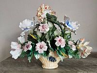 Front view of the colorful porcelain flower bouquet showing various flowers and green leaves in a cream-colored ceramic basket base with blue sticker.