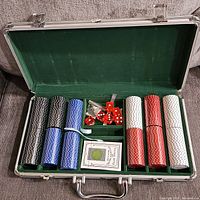 Open poker set in aluminum case showing neatly arranged stacks of poker chips in black, blue, red, and white.