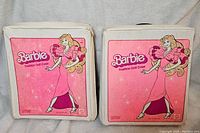 Front view of two white Barbie Fashion Doll Cases with pink illustrated Barbie on the front. Both show moderate wear but are intact.