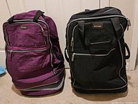 Pair of foldable rolling luggage bags, purple and black, standing upright side-by-side showing front and side views