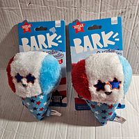 Two plush dog toys in patriotic red, white, and blue colors shaped like ice cream cones with star-shaped sunglasses, in original packaging.