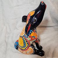 Side view of the Talavera pottery howling coyote statue showing colorful floral and geometric patterns on a glossy black background