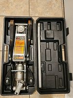 Floor jack inside black carrying case with handle removed, visible rust on jack surface