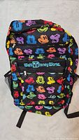 Front view of black backpack with multicolored Mickey Mouse faces and Walt Disney World branding on front pocket.