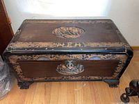 Front view of the entire wooden chest showing intricate carved details, brass latch, and claw-like feet.