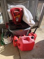 Various auto supplies including red gas cans, PowerPack 12V battery charger, white car cover, and toolbox in a gray container.