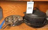 Cast iron Dutch oven stacked with two cast iron skillets and one pan with round indentations, showing signs of rust and wear