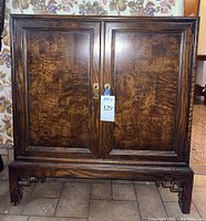 Front view of Chinoiserie style wooden cabinet with double doors showing unique wood grain pattern and metal pulls.